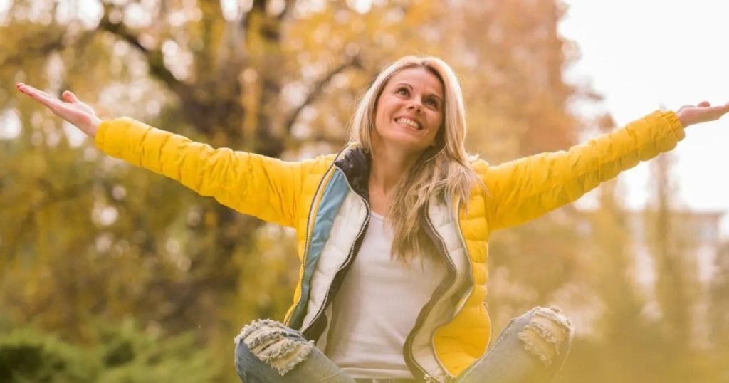 Happy woman with open arms sitting in nature, feeling calm and confident after releasing her fears