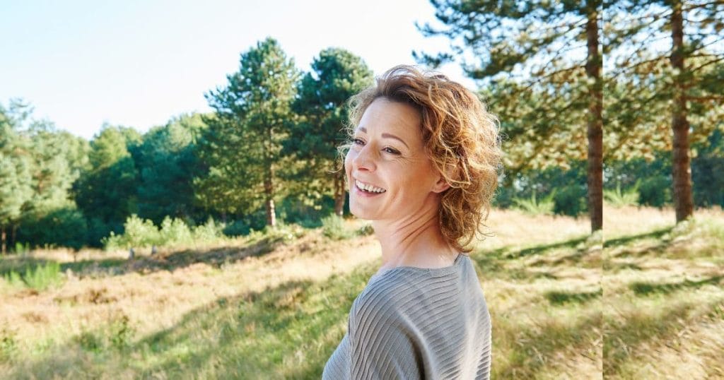 Smiling woman in nature, feeling calm and happy after hypnotherapy