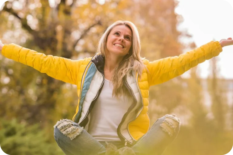 Happy woman with open arms sitting in nature, feeling calm and confident after releasing her fears