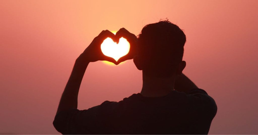 Man holding hands in heart shape toward sunrise, representing inner confidence and mindset transformation through hypnotherapy