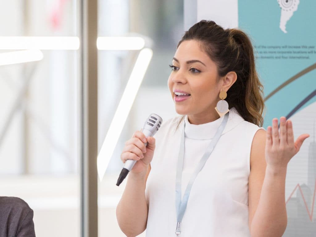 Confident woman speaking into a microphone to an audience, showing how RTT® Hypnotherapy builds self-assurance