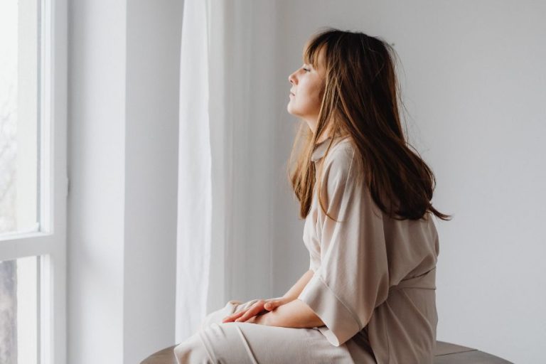 Person sitting near a window with soft light, looking upward with a peaceful, reflective expression.