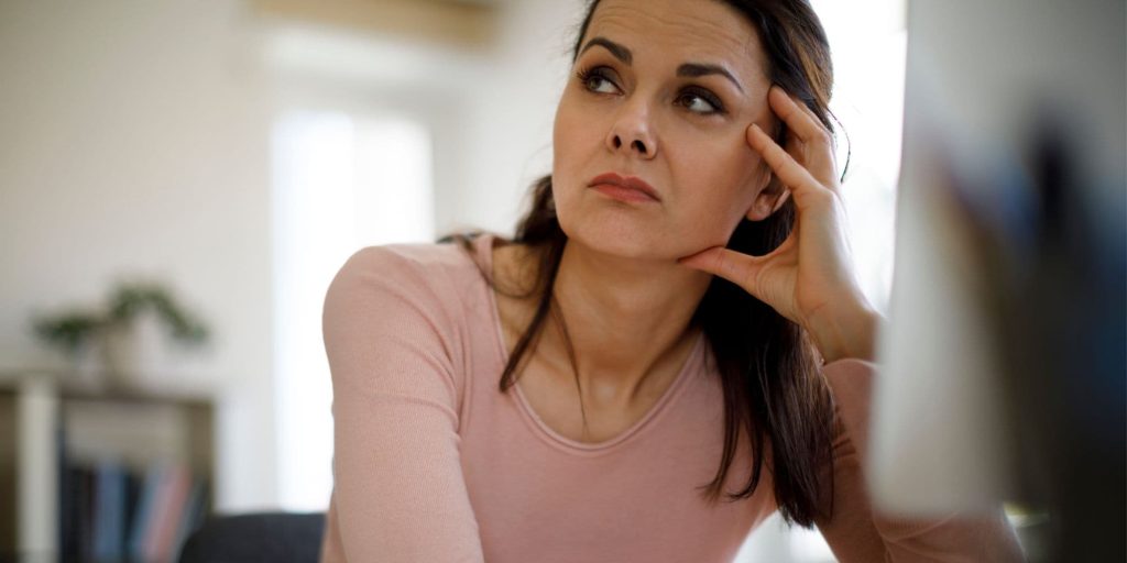 Woman sitting at her desk with a thoughtful, slightly worried expression, recognising a familiar fear‑based reaction.