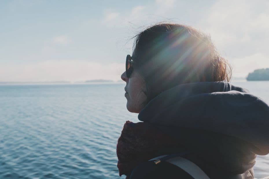 A person sitting near the water, looking thoughtful and slightly withdrawn, reflecting the quiet signs of overwhelm.