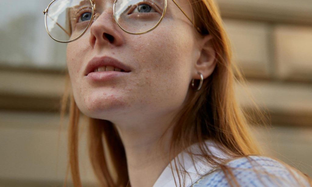 Close-up of a thoughtful woman with glasses looking upward, symbolising reflection and self-kindness