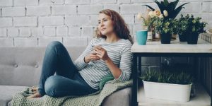 A woman sitting on a sofa in a quiet indoor setting, looking down at her phone with a calm, thoughtful expression.